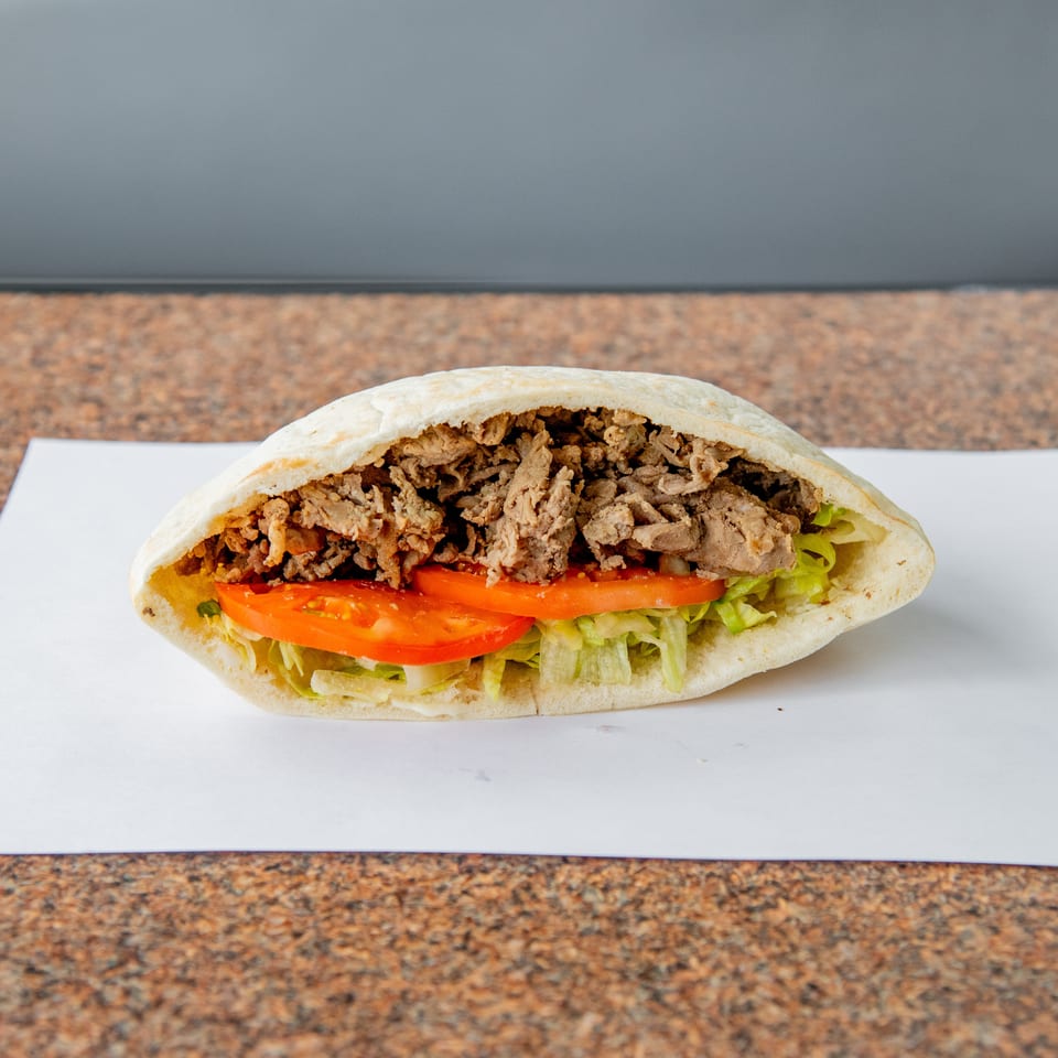 Chicken shawarma sandwich in pita bread with sliced tomatoes and lettuce, served on white paper.