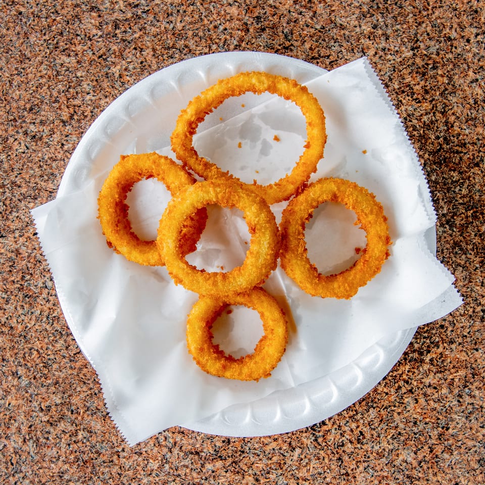Golden-brown crispy onion rings arranged on a paper-lined white plate atop a speckled countertop.