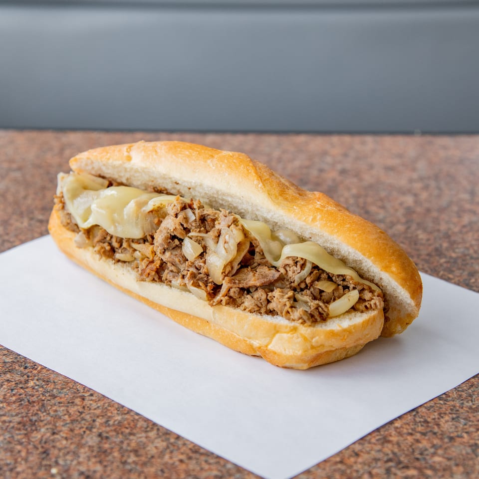 Steak sandwich with melted cheese and onions on a toasted roll, served on white paper atop a speckled countertop.