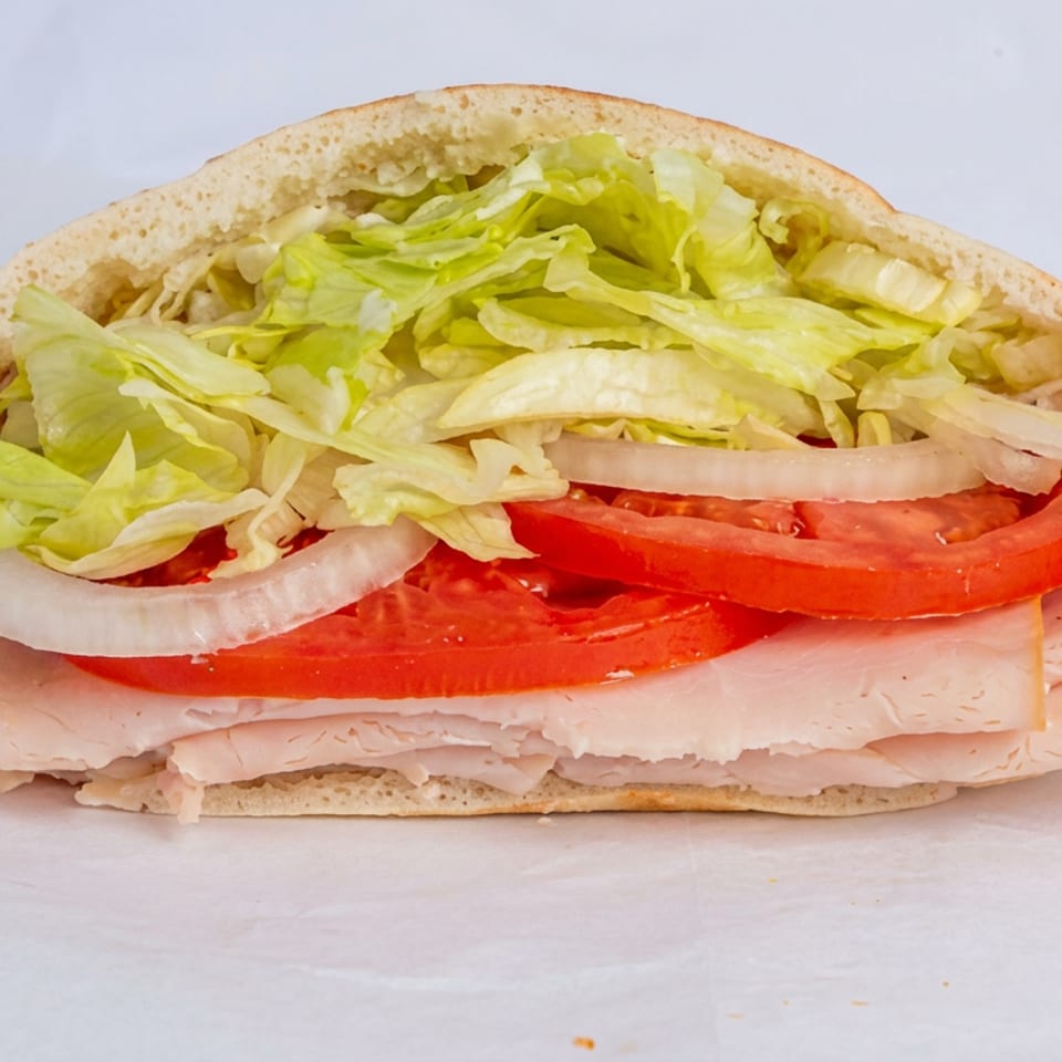 Pita sandwich filled with sliced turkey, tomatoes, onions, and shredded lettuce on a light background.
